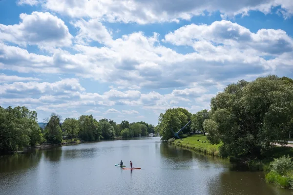 Die Fulda in Kassel von der Drahtbrücke aus, rechts die Skulptur Spitzhacke am Ufer, auf dem Wasser zwei Stand-up-Paddler.