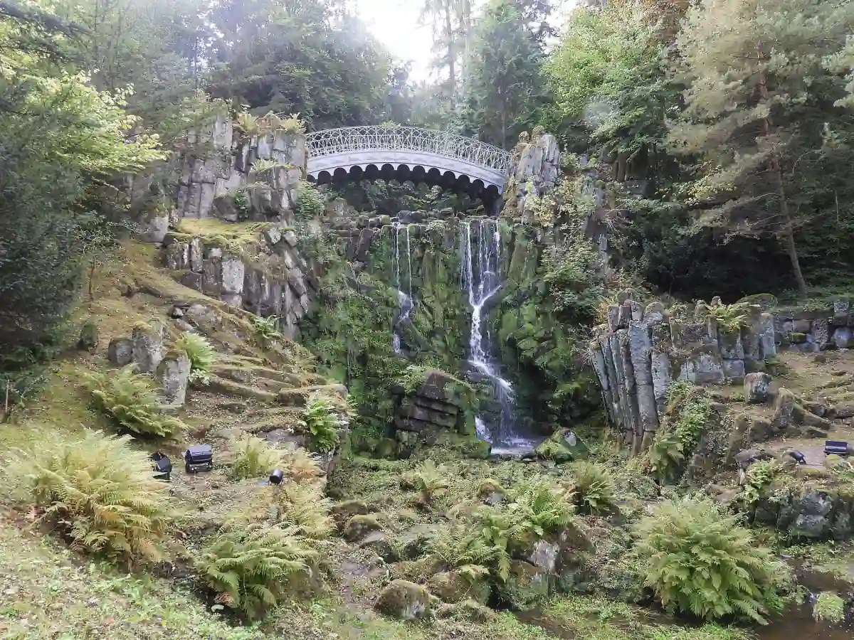 Die Teufelsbrücke spannt sich über einen Wasserfall in einer bewachsenen Felsschlucht im Bergpark Wilhelmshöhe.